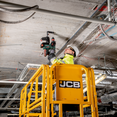 Homem a perfurar teto de betão com furadeira Metabo numa plataforma JCB amarela
