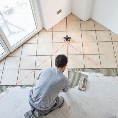 Pessoa a colocar azulejos quadrados bege numa parede branca