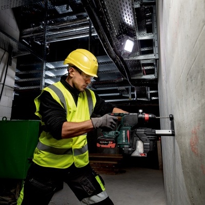 Homem a usar furadeira numa parede de cimento num ambiente industrial