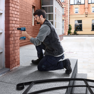 Homem ajoelhado a usar furadeira Bosch num muro de tijolos vermelhos exterior
