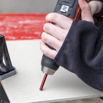 mão com luva a usar ferramenta elétrica numa superfície branca