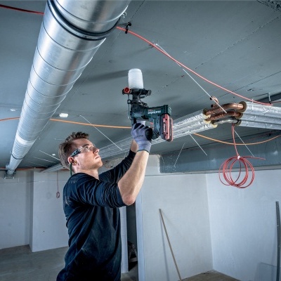 Homem com ferramenta elétrica a trabalhar no teto numa sala industrial