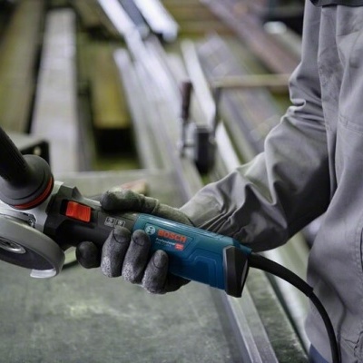 Máquina de corte Bosch azul e preta segurada por pessoa com luvas cinzentas em ambiente industrial