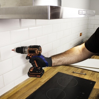 Pessoa a usar parafusadeira elétrica numa parede de azulejos numa cozinha moderna com bancada de madeira e placa de fogão