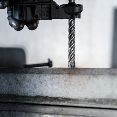 Broca metálica numa furadeira azul a perfurar betão cinzento