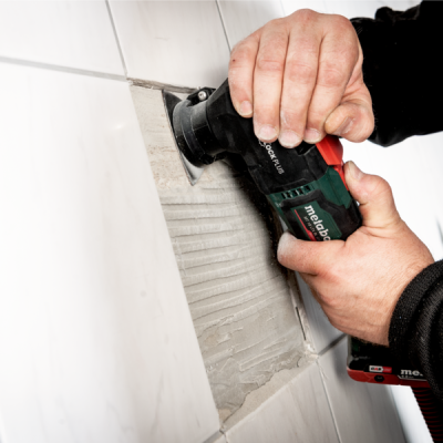 Pessoa a usar máquina Metabo para retirar azulejos numa parede branca