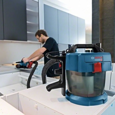 Aspirador portátil azul BOSH ligado a ferramenta elétrica em cozinha moderna branca com armários cinzentos.