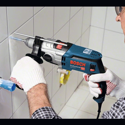 Pessoa a usar broca elétrica BOSCH para furar azulejo branco na parede