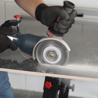 Máquina de corte elétrica a cortar superfície cinzenta brilhante com mãos de luva preta