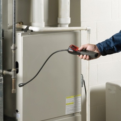 Caldeira cinza com tubos, pessoa a inspecionar com ferramenta preta e vermelha