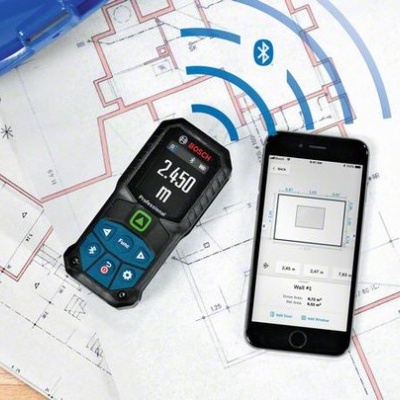 Medidor laser Bosch preto e smartphone sobre plantas arquitetónicas em papel sobre mesa de madeira com capacete azul