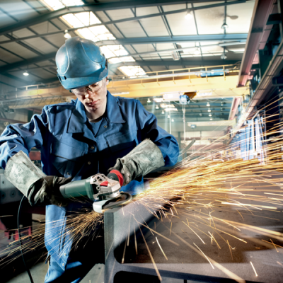 Trabalhador em fato de proteção a usar rebarbadora e faíscas numa oficina industrial