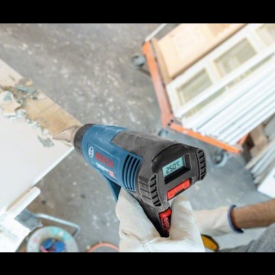 Pistola de ar quente Bosch azul e preta com visor digital a mostrar 250°C em ambiente de construção