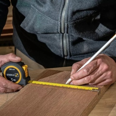 Pessoa a medir madeira com fita métrica STANLEY e lápis branco numa oficina