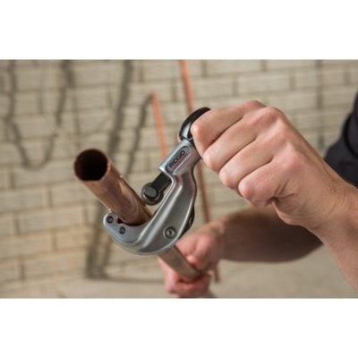 Corte de tubo de cobre com ferramenta com punho preto em parede de azulejo bege