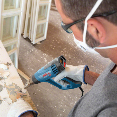 Homem usa pistola de ar quente Bosch azul e preta para remover pintura