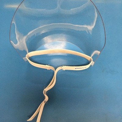 Visor facial transparente com fita branca sobre superfície azul