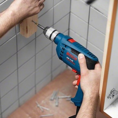 Furadeira elétrica azul Bosch a aparafusar madeira em parede de azulejos brancos