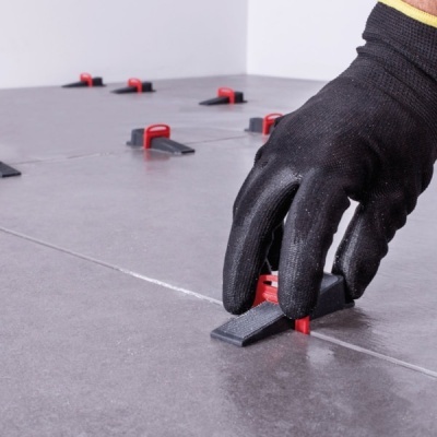 Mão com luva preta posiciona espaçador entre azulejos cinzentos