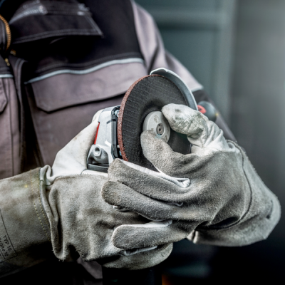 Pessoa segurando rebarbadora com luvas de proteção em ambiente de trabalho