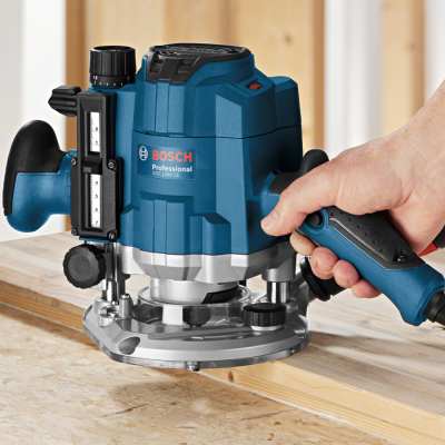 Tupia elétrica Bosch Professional GOF 1250 CE em madeira, com mão segurando a ferramenta