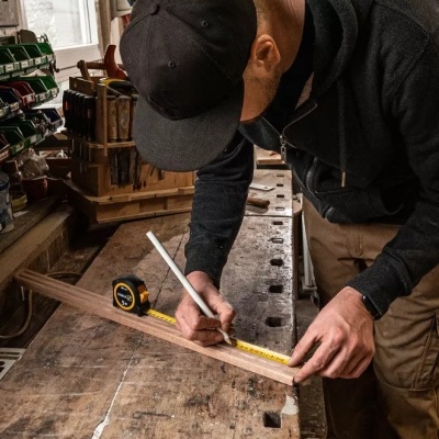 Homem numa oficina de carpintaria a medir régua amarela sobre bancada de madeira
