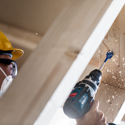 Trabalhador a usar capacete e máscara a furar madeira com furadeira