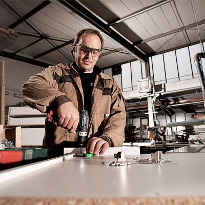 Homem com óculos de segurança e casaco a usar furadeira num ambiente industrial