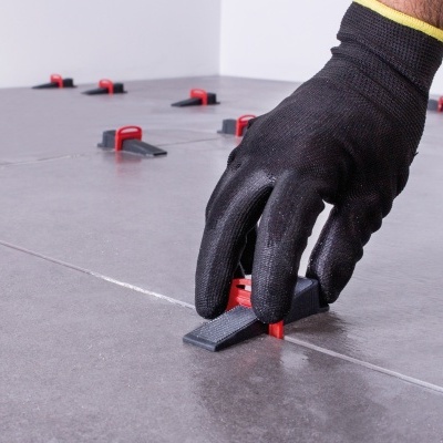 Mão enluvada a ajustar sistema de nivelamento em azulejos cinza com espaçadores pretos e vermelhos