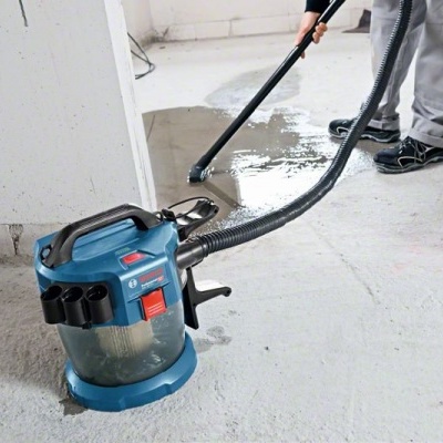 Aspirador industrial azul a aspirar água num piso interior branco e cinzento