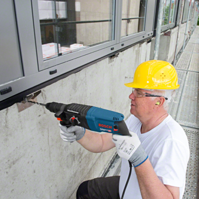 Homem com capacete amarelo usando furadeira BOSCH numa parede junto a janela