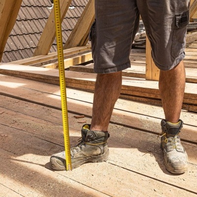 Pernas de pessoa com calções e botas em obra de madeira com fita métrica amarela