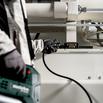 Pessoa a usar ferramenta elétrica Metabo em ambiente industrial com tubos brancos