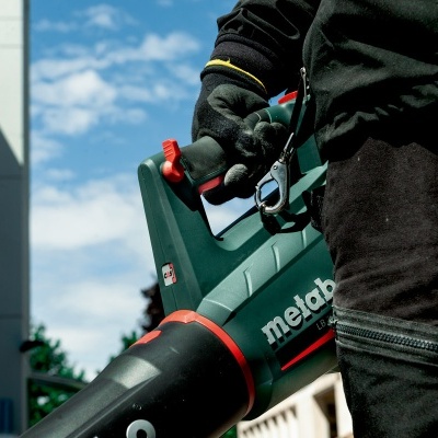 Soprador de folhas Metabo verde escuro com punho preto segurado por pessoa com roupa preta e verde