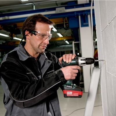 Pessoa a operar furadeira elétrica numa parede de blocos num espaço industrial