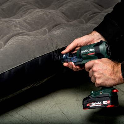Ferramenta elétrica Metabo a ser usada para reparar tecido preto num colchão cinzento.