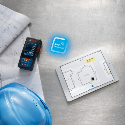 Mesa com capacete azul, dispositivo Bosch de medição com ecrã, planta baixa em papel e tablet com planta digital