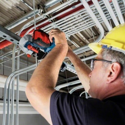 Trabalhador com capacete usando ferramenta elétrica para trabalhar em tubulação no teto
