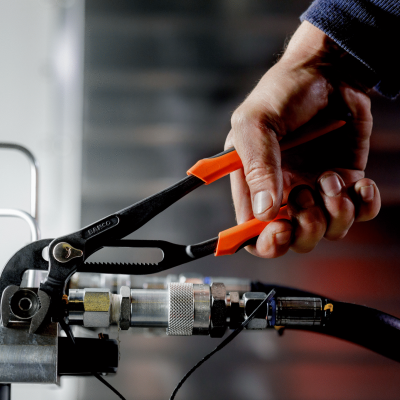 Alicate preto com cabo laranja a ser usado numa peça metálica em oficina