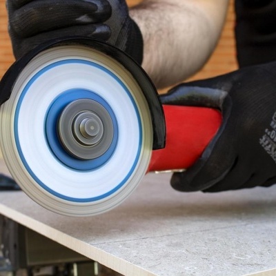 Ferramenta elétrica de esmeril com disco azul e punho vermelho em uso