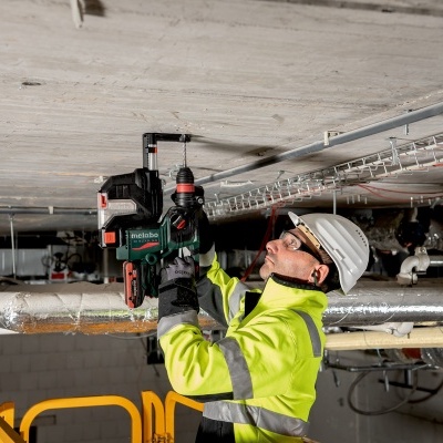 Trabalhador com capacete branco e casaco amarelo a usar ferramenta Makita no teto de construção