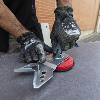 Mãos com luvas cinzentas a montar peça metálica prateada sobre superfície cinzenta e vermelha