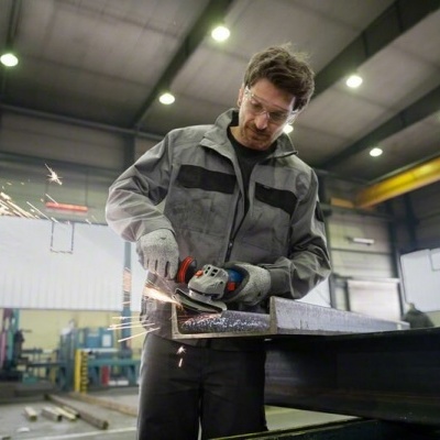 Homem a cortar peça metálica com rebarbadora elétrica numa oficina industrial