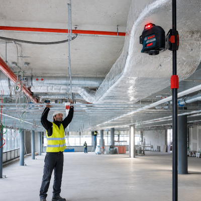 Laser de construção BOSCH Professional em tripé num espaço industrial em construção com trabalhador a ajustar teto