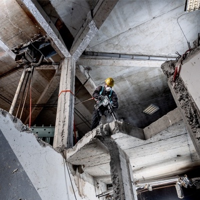 Homem com capacete amarelo e equipamento de segurança em obra interior de cimento com vigas, pilares e laje partida