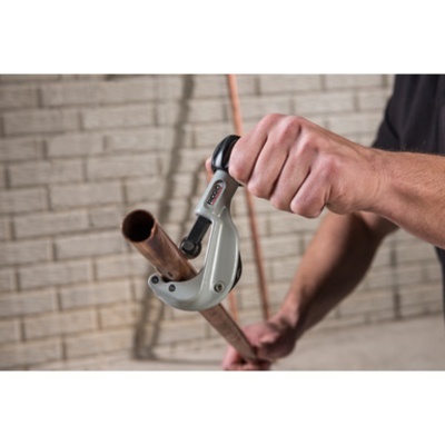 Mão a usar cortador de tubos metálicos para cortar tubo de cobre