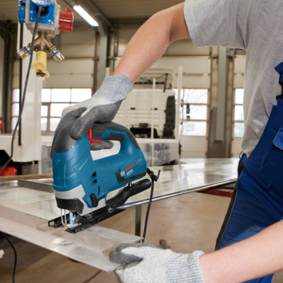 Máquina de recortes elétrica BOSCH azul em uso com luvas cinzentas em ambiente industrial