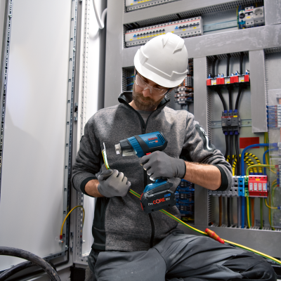 Trabalhador com capacete a usar ferramenta elétrica BOSCH num painel elétrico