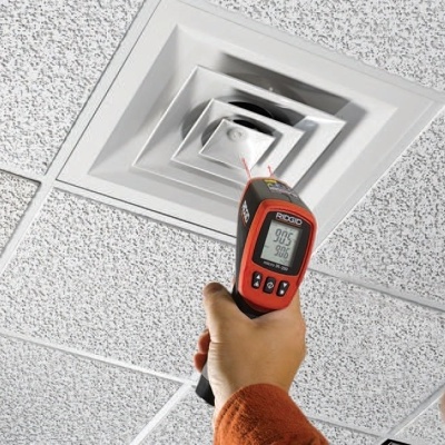 Dispositivo de medição infravermelho a apontar para uma grelha de ventilação num teto branco.