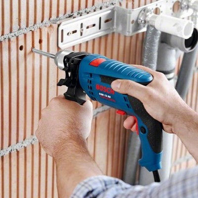 Pessoa a usar furadeira elétrica BOSCH GSB 10 RE numa parede de tijolos